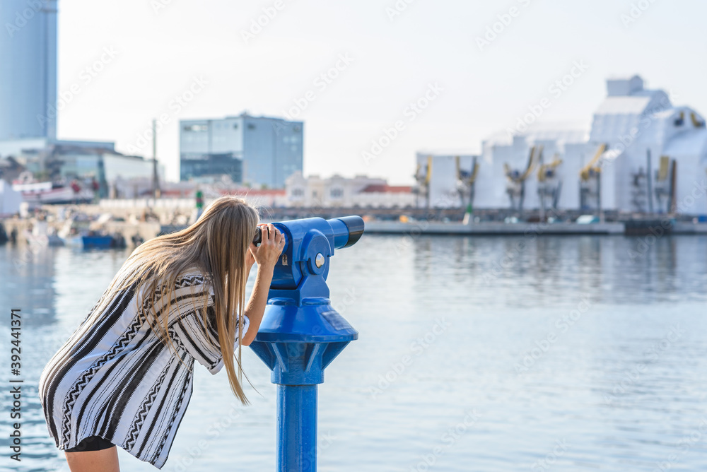 young slim caucasian blonde woman wearing casual clothes and using spyglass on a sea port