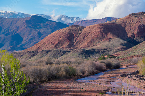 Daytime wide angle shot of Beautiful landscape of snow capped mountains and bushes and a riachuelo in the valley. Atlas  Morocco.