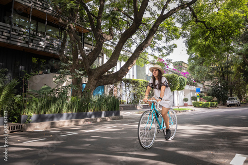 Wallpaper Mural Mujer paseando en bicicleta en la calle con arboles a los lados. Mujer usando vestido blanco y sombrero mientras pasea en bici. Torontodigital.ca