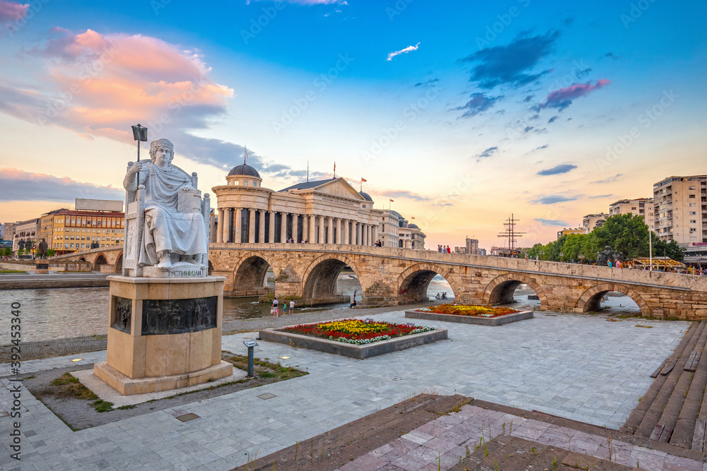 SKOPJE, NORTH MACEDONIA - 01.08.2020: Byzantine Emperor Justinian Statue and Stone Bridge, behind the Archeology Museum at sunset in Skopje