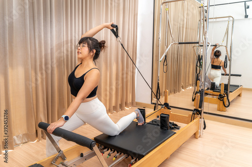 Young Asian woman working on pilates reformer machine during her health exercise