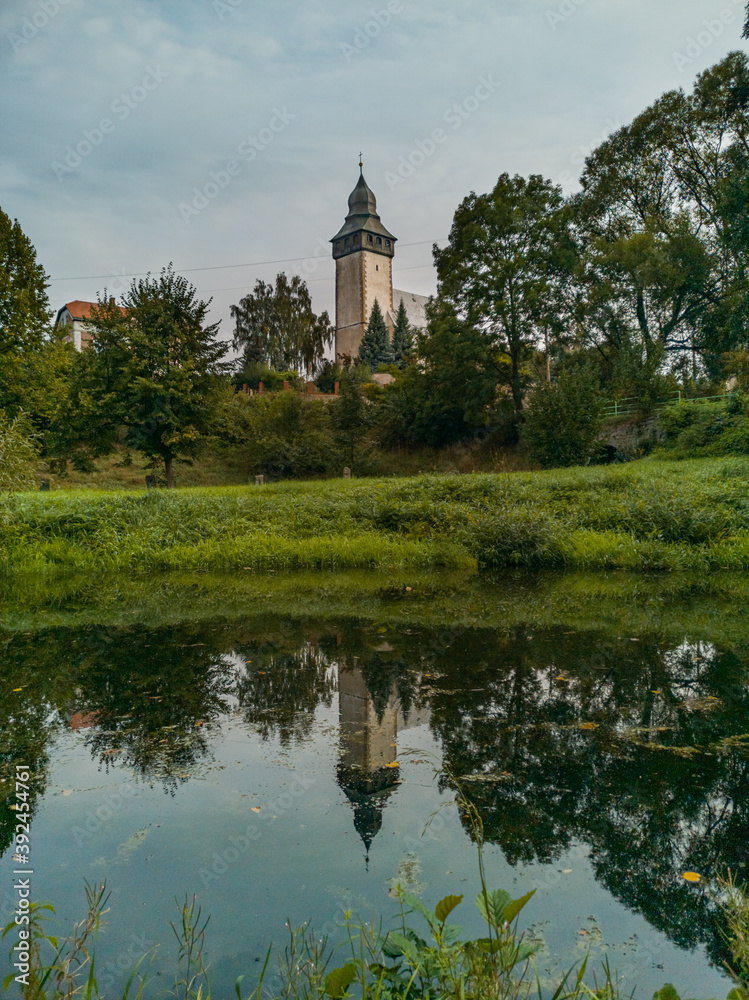 Church tower behind park reflecting in small calm river