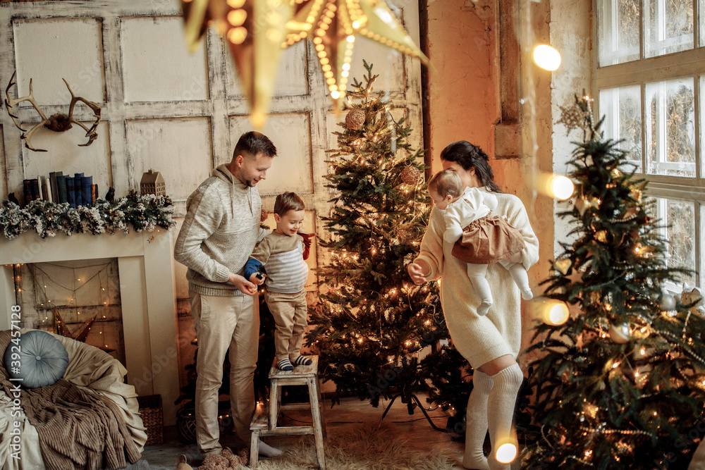 Caring parents with little kids decorate the Christmas tree, beautiful mother hold adorable daughter in arms, smiling, happy family spend winter holidays together, xmas concept
