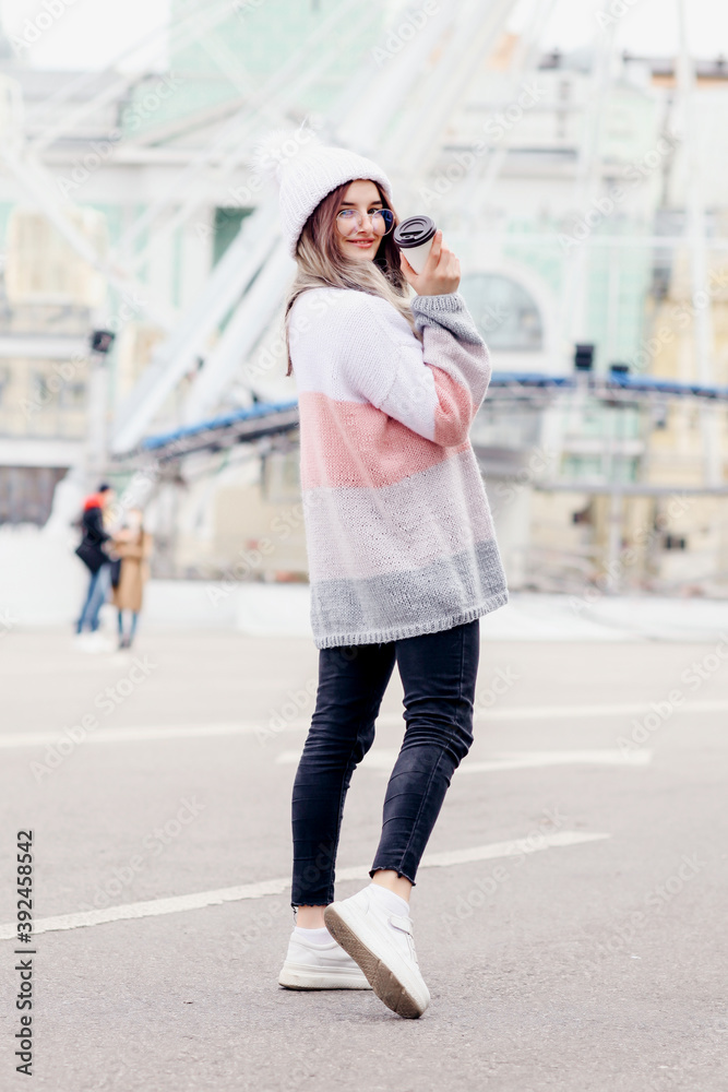 Beautiful girl posing on the street in cold winter, she has coffee in hands, smiling and having fun alone