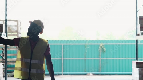 African America engineer wearing safety helmet and vest open the warehouse door and walk in the automotive parts warehouse area and say hello to his collogue. Inventory and management concept photo