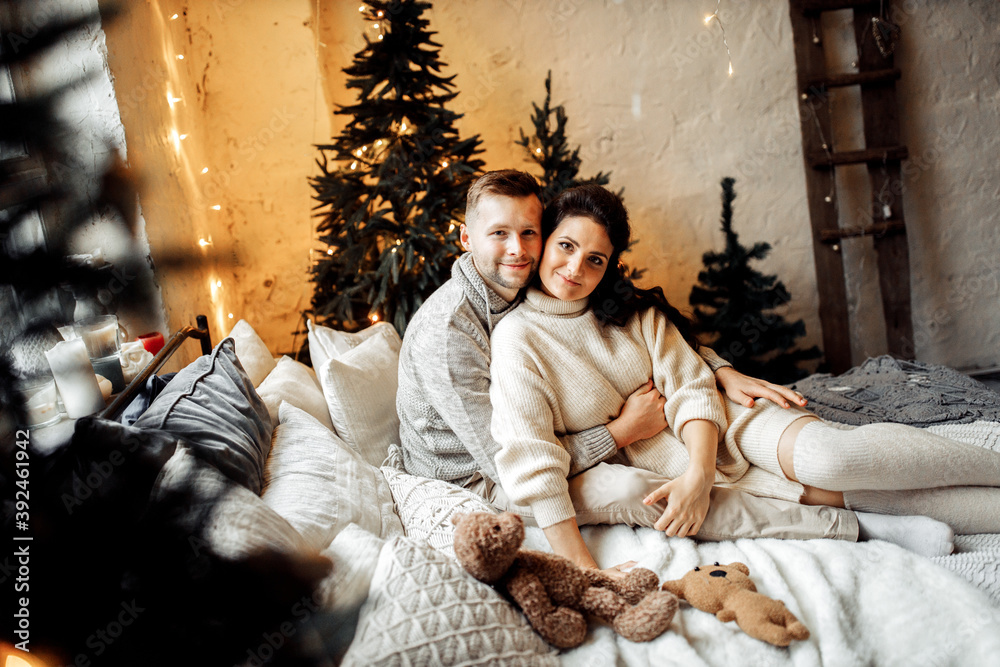 Happy couple cuddling at the bed at home, smiling, charming husband with gorgeous wife spend winter holidays together, enjoy Christmas morning, New Year celebration concept
