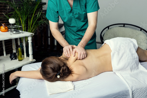 The hands of a male masseur doing massage of a young woman. Beautiful relaxed face of a young woman with brown hair