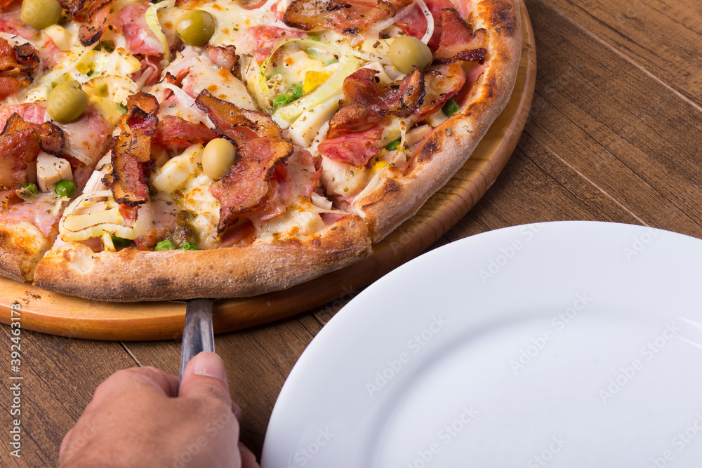 Portuguese pizza made with ham, pea egg, heart of palm, pepperoni, onion and mozzarella and bacon. Serving slice of pizza with spatula. Gastronomic photography of restaurants and pizzerias. Portuguese pizza made with ham, pea egg, heart of palm, pepperoni, onion and mozzarella and bacon. Serving slice of pizza with spatula. Gastronomic photography of restaurants and pizzerias.