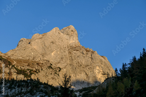 Clear morning in Hochschwab region in Austrian Alps. Very gentle sunrise color. Sun beams reaching the highest parts of the mountains. Dense forest in front. Sharp and steep Alpine slopes.