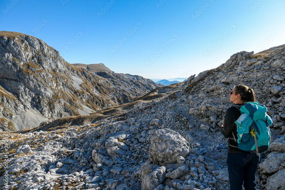 A woman hiking in Hochschwab region in Austrian Alps. Steep mountain chain in front of her. Massive Alps. Autumn vibes in the mountains. Idyllic landscape. Freedom and wilderness