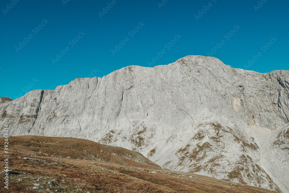 A panoramic view on the plain on top of a mountain in Hochschwab region in Austrian Alps. The flora overgrowing the slopes is turning golden. Autumn vibes. Many mountain chains in the back. Wilderness