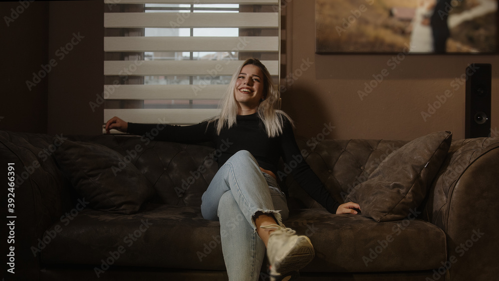 Beautiful happy young blonde woman smiling and sitting on sofa she is very happy and joyful! Home and relaxation concept