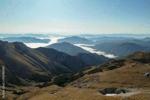 A panoramic view on the plain on top of a mountain in Hochschwab region in Austrian Alps. The flora overgrowing the slopes is turning golden. The valley is shrouded in fog. Mysterious landscape