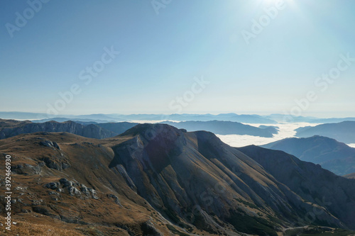 A panoramic view on the plain on top of a mountain in Hochschwab region in Austrian Alps. The flora overgrowing the slopes is turning golden. The valley is shrouded in fog. Mysterious landscape