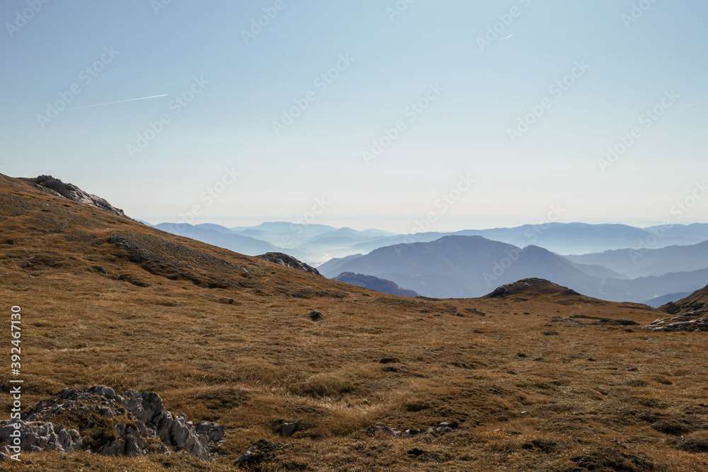 A panoramic view on the plain on top of a mountain in Hochschwab region in Austrian Alps. The flora overgrowing the slopes is turning golden. Autumn vibes. Many mountain chains in the back. Wilderness