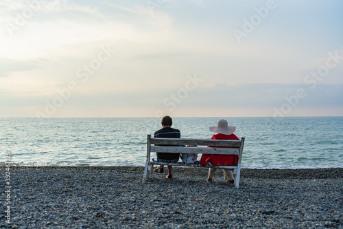 a man and a woman sit on a bench by the Black Sea and watch the sunset