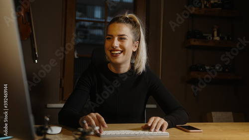Young blond beautiful woman dressed in black spends time on the computer at the desk in the office, Office worker concept
