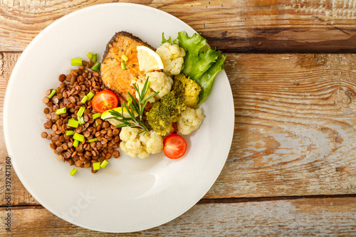 Baked fish with broccoli and lentils in a beige plate with rosemary and green onions.