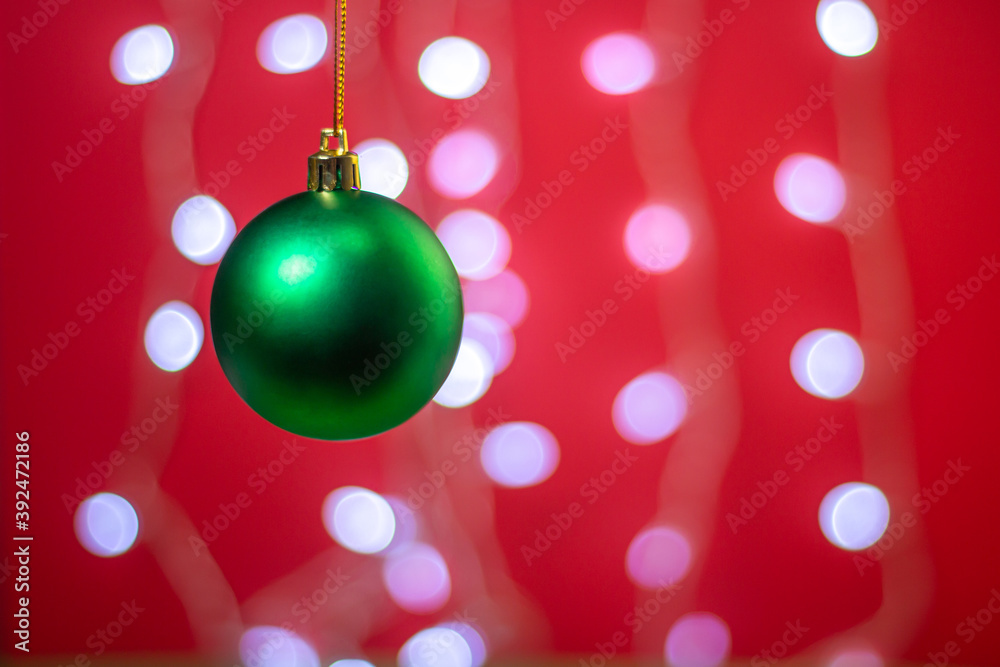 Green Christmas ball on a background of a glowing garland. Christmas decorations on a red background. Holiday decorations. Christmas concept. Green Christmas ball on a background of a glowing garland. Christmas decorations on a red background. Holiday decorations. Christmas concept.
