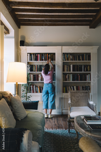 Bild auf Leinwand Girl looking for a book in bookcase in a rustic living room at evening