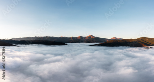 Foggy mountain landscape above the clouds at sunset. Aerial view.