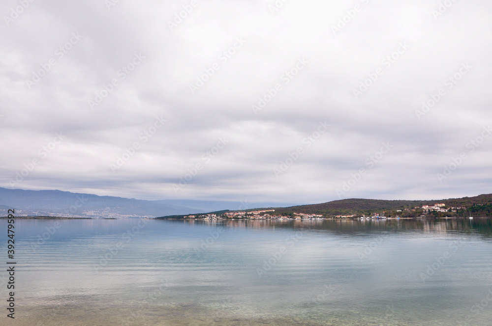 Island Krk sand beach with Velebit mountain in background. Calm Adriatic Sea. Croatian coastline.
