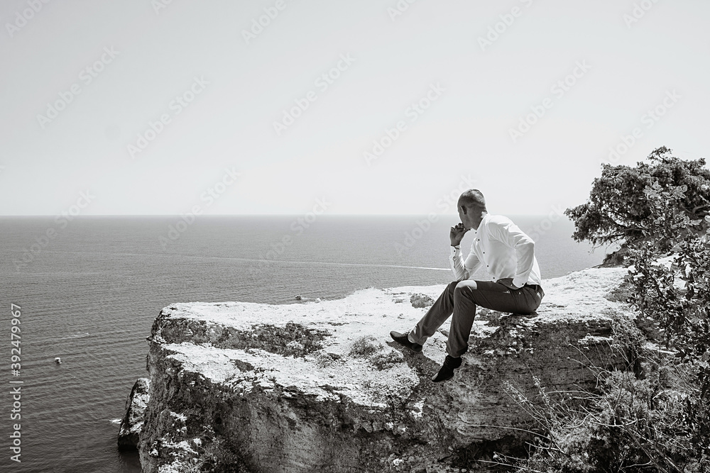 Fototapeta premium A pensive young man sits at a cliff. Portrait of a guy by the sea.