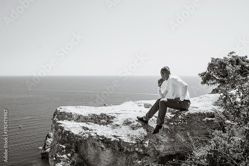 A pensive young man sits at a cliff. Portrait of a guy by the sea.