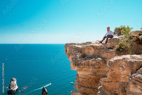 A pensive young man sits at a cliff. Portrait of a guy by the sea.