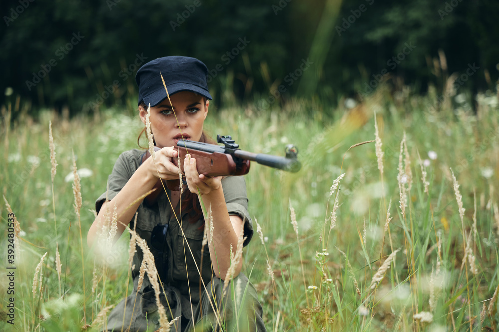 Fototapeta premium Military woman Shelter sits on the grass hunting weapon green leaves