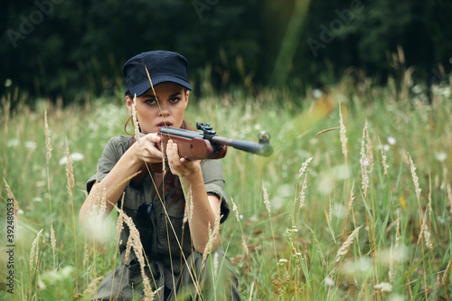 Military woman Shelter sits on the grass hunting weapon green leaves