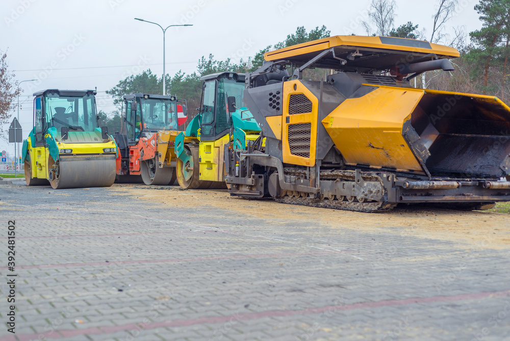 Asphalt paver machine and steam road roller during road construction and repairing works, process of asphalting and paving, workers working on the new road construction site