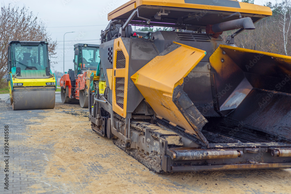 Asphalt paver machine and steam road roller during road construction and repairing works, process of asphalting and paving, workers working on the new road construction site Asphalt paver machine and steam road roller during road construction and repairing works, process of asphalting and paving, workers working on the new road construction site