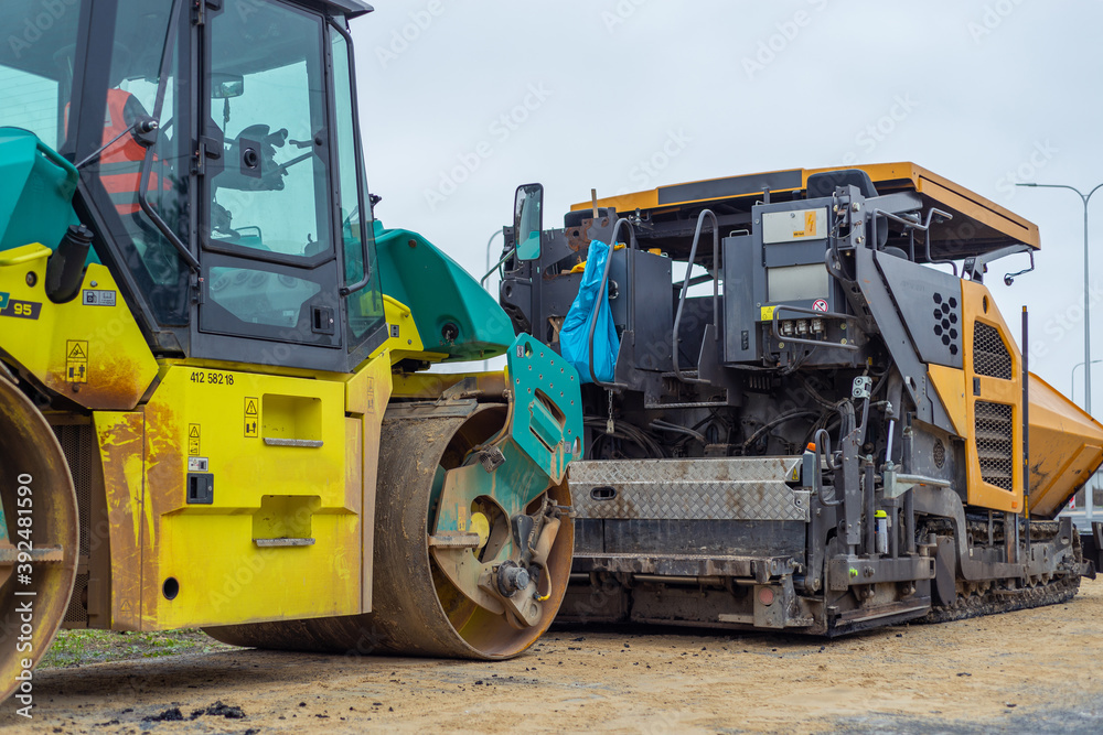 Asphalt paver machine and steam road roller during road construction and repairing works, process of asphalting and paving, workers working on the new road construction site