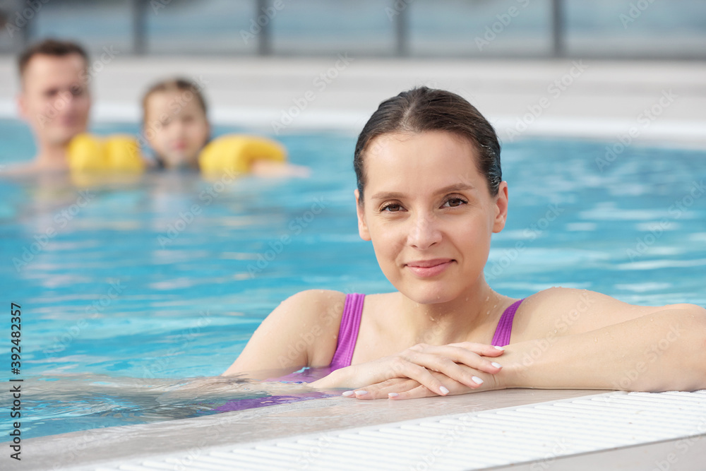 Happy young brunette female in lilac swimwear standing in swimming pool