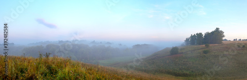 Tranquil summer landscape with green hills and trees during foggy morning