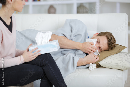 man laying on sofa blowing his nose partner holding tissues