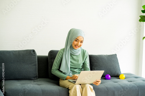 Asian Muslim young attractive businesswoman mother wearing green HIJAB headscarf work from home and caring baby girls. new normal concept. 