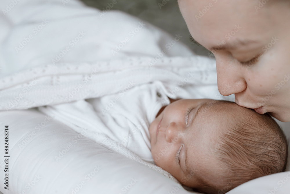 Adorable child in a white sunny bedroom. Baby is resting in bed. Family morning at home. Loving mom carying of her newborn baby. Adorable child in a white sunny bedroom. Baby is resting in bed. Family morning at home. Loving mom carying of her newborn baby.