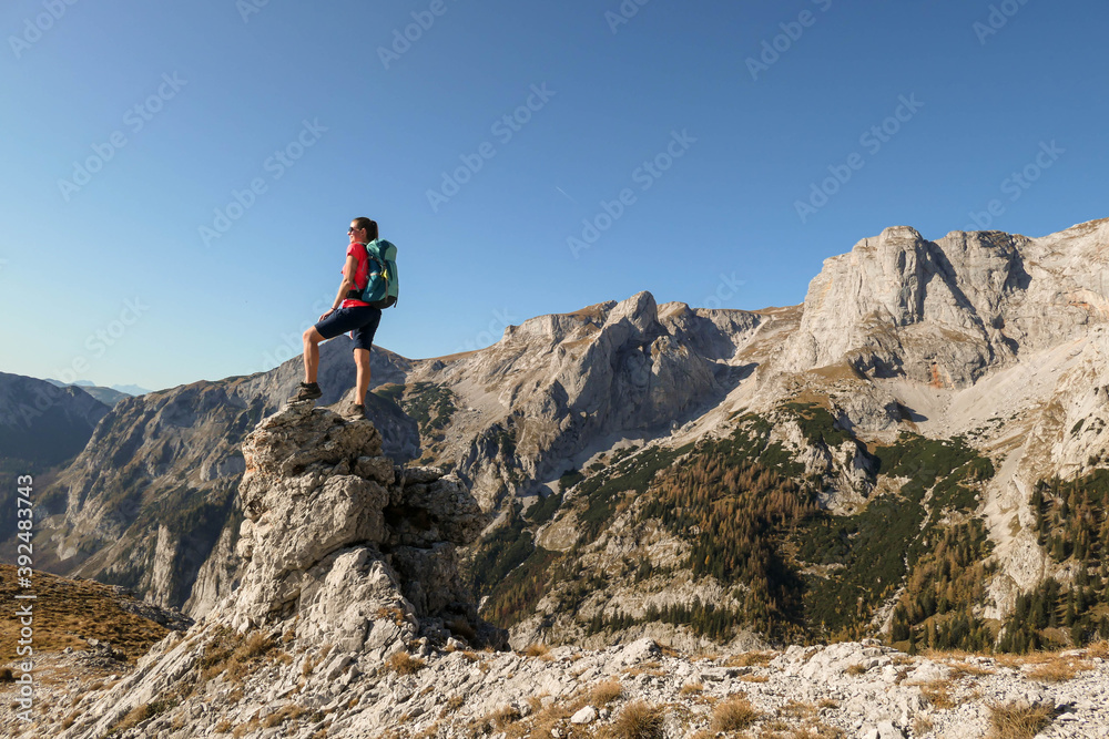 Woman standing on top of a sharp, pointy boulder in Hochschwab region, Austrian Alps. The steep mountain wall in front look very dangerous. High mountaineering. Autumn vibes. Adventure and freedom