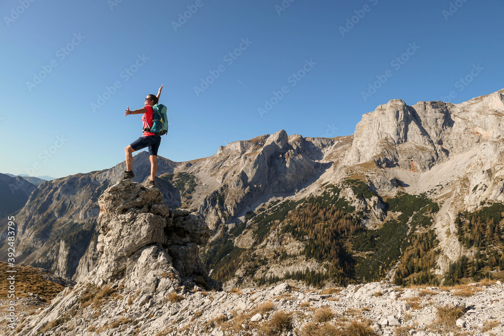 Fototapeta premium Woman standing on top of a sharp, pointy boulder in Hochschwab region, Austrian Alps. The steep mountain wall in front look very dangerous. High mountaineering. Autumn vibes. Adventure and freedom
