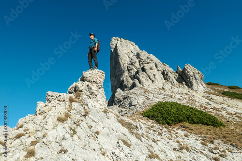 A man standing on top of a sharp, pointy boulder in Hochschwab region, Austrian Alps. The steep mountain wall in front look very dangerous. High mountaineering. Autumn vibes. Adventure and freedom