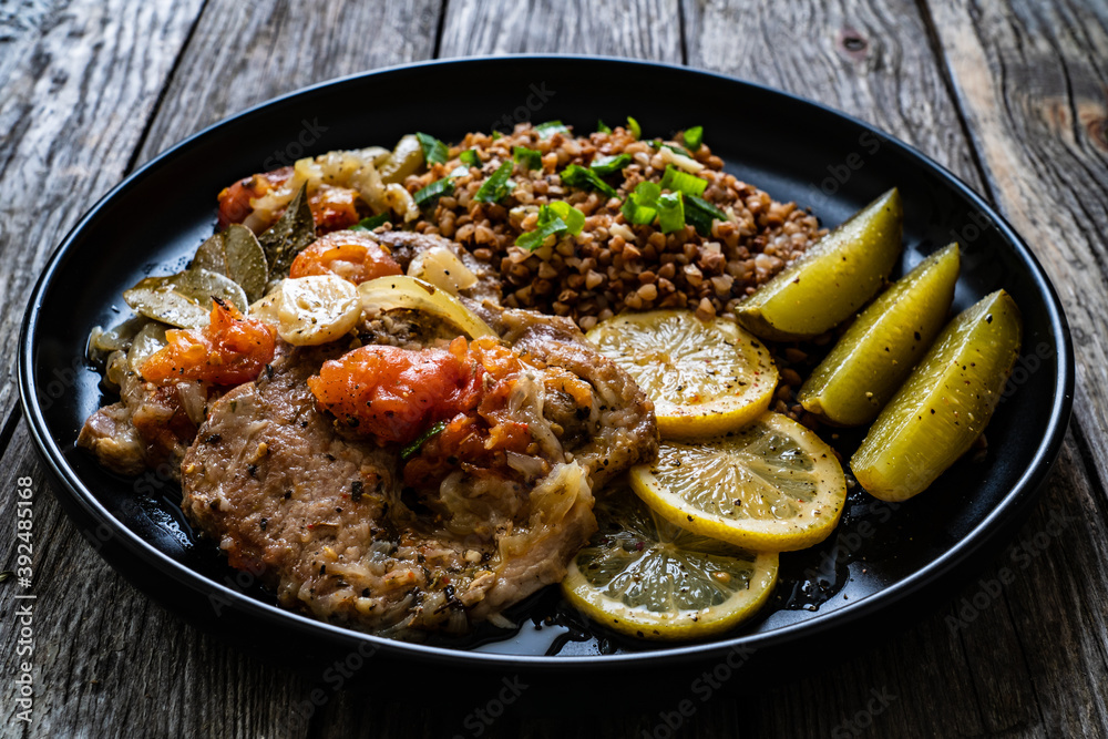 Roasted meat, buckwheat and pickled cucumbers lemon and toamtoes on wooden table
