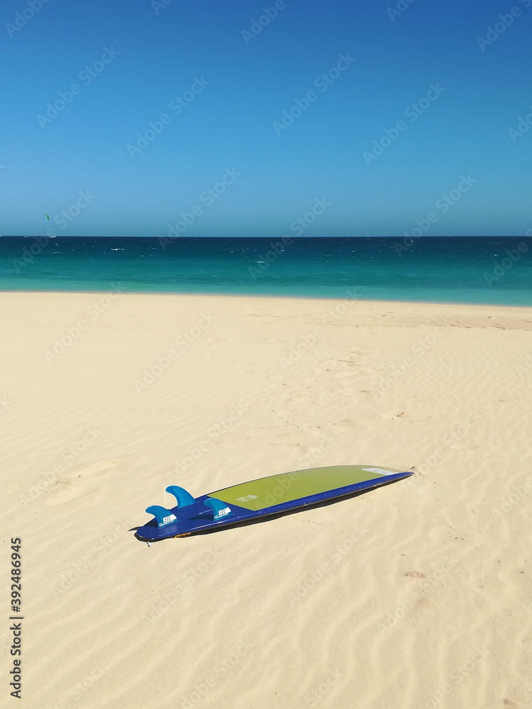 Yellow and blue surfboard resting on the sand Yellow and blue surfboard resting on the sand