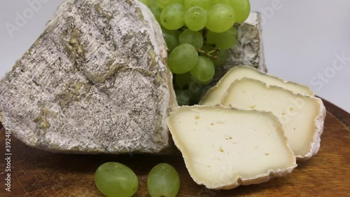 A plate of assorted mouldy goat's milk cheeses on a wooden Board with green grapes
