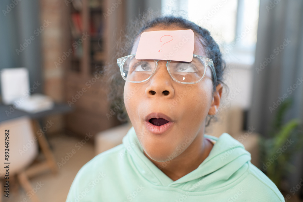 Girl in eyeglasses looking at notepaper with question mark on her forehead Girl in eyeglasses looking at notepaper with question mark on her forehead