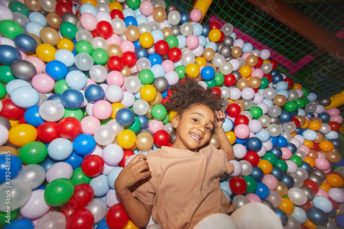Portrait of African happy little girl lying among colored balls in dry pool