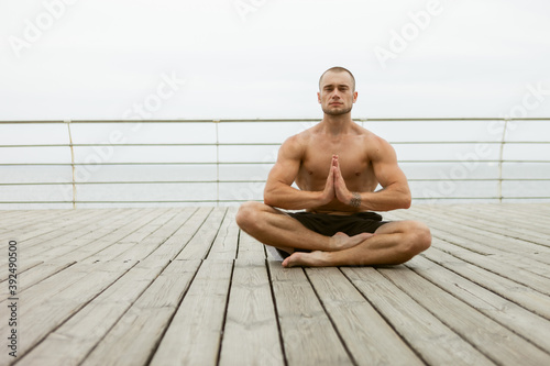 Muscular athlete man with a naked torso meditates on the beach. Practicing yoga hatha