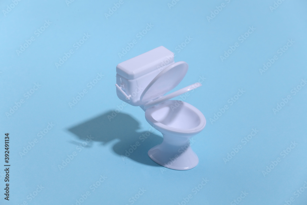 Mini white toilet on blue background with deep shadow. Minimalism. Mini white toilet on blue background with deep shadow. Minimalism.