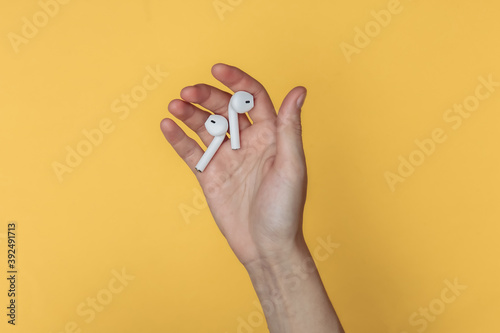 Wireless headphones in a female palm on a yellow background